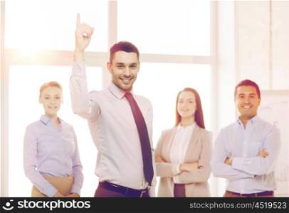 business and office concept - smiling handsome businessman with team in office and finger up. smiling businessman in office with team on back