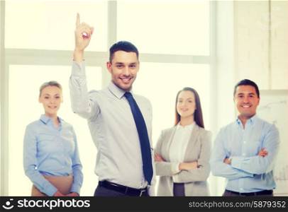business and office concept - smiling handsome businessman with team in office and finger up. smiling businessman in office with team on back