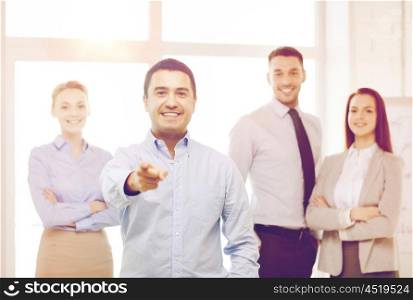 business and office concept - smiling handsome businessman with team in office pointing finger at you. businessman in office pointing finger at you