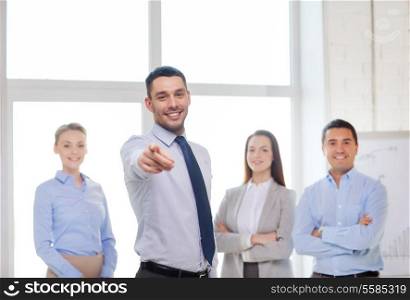 business and office concept - smiling handsome businessman with team in office pointing finger at you