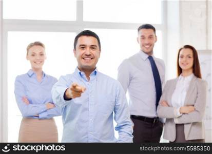 business and office concept - smiling handsome businessman with team in office pointing finger at you