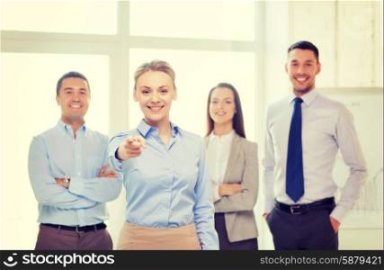business and office concept - smiling handsome businesswoman with team in office pointing finger at you. businesswoman in office pointing finger at you