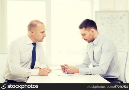 business and office concept - two serious businessman with papers in office