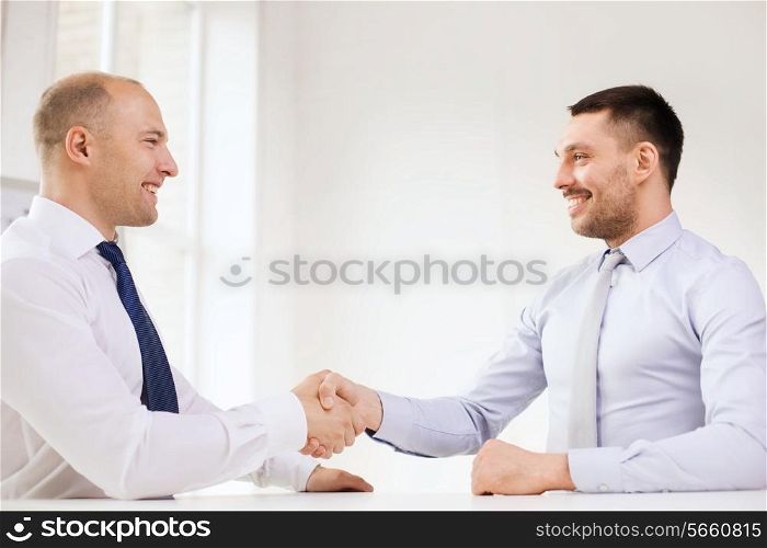 business and office concept - two smiling businessmen shaking hands in office