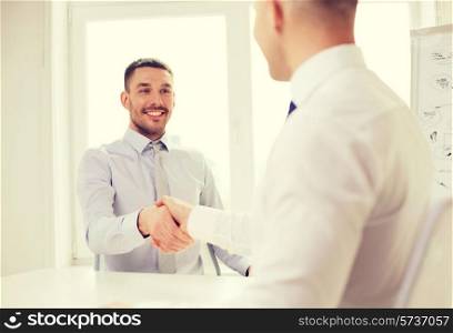business and office concept - two smiling businessmen shaking hands in office