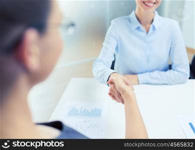 business and office concept - two smiling businesswoman shaking hands in office. two smiling businesswoman shaking hands in office