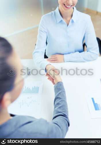 business and office concept - two smiling businesswoman shaking hands in office. two smiling businesswoman shaking hands in office