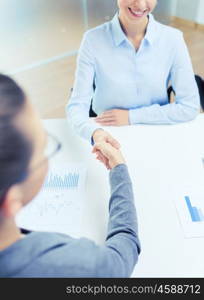 business and office concept - two smiling businesswoman shaking hands in office. two smiling businesswoman shaking hands in office