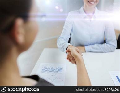 business and office concept - two smiling businesswoman shaking hands in office. two smiling businesswoman shaking hands in office