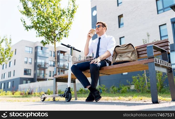business and people and concept - young businessman with bag and electric scooter sitting on street bench and drinking coffee from takeaway paper cup in city. businessman with scooter drinking coffee in city