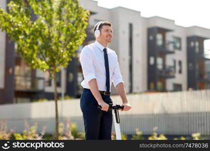 business and people and concept - young businessman with headphones riding scooter and listening to music in city. businessman with headphones riding scooter in city