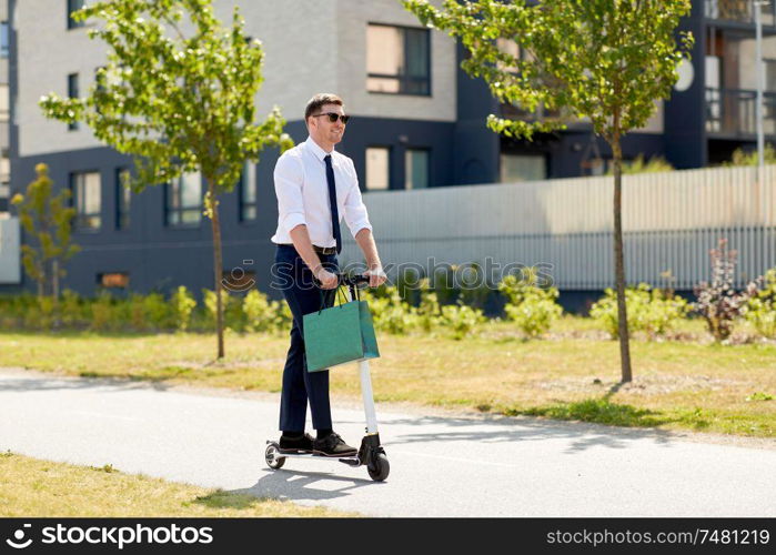 business and people and concept - young businessman with shopping bag riding electric scooter outdoors. businessman with shopping bag riding scooter