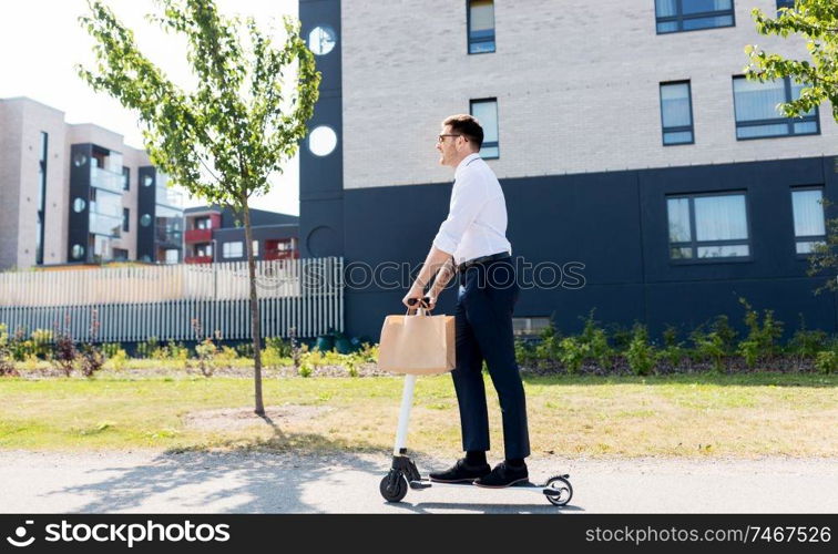 business and people and concept - young businessman with takeaway lunch in paper bag riding electric scooter outdoors. businessman with takeaway lunch riding scooter