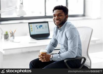 business and people concept - african american businessman with coffee sitting at office table. african american businessman with coffee at office. african american businessman with coffee at office