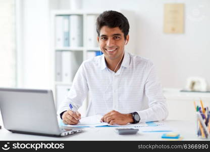 business and people concept - businessman in earphones with papers and laptop computer working at office and listening to music. businessman in earphones working at office