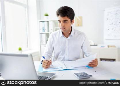 business and people concept - businessman in earphones with papers and laptop computer working at office and listening to music. businessman in earphones working at office