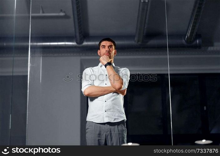 business and people concept - businessman looking at glass wall at night office. businessman looking at glass wall at night office