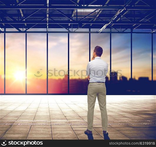 business and people concept - businessman thinking over empty office room and city view background. businessman thinking over office and city view