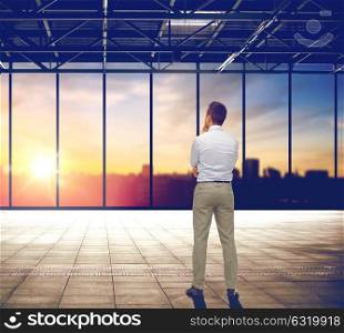 business and people concept - businessman thinking over empty office room and city view background. businessman thinking over office and city view