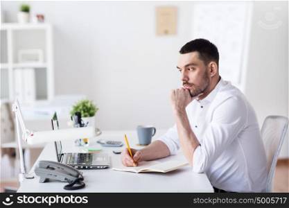 business and people concept - businessman with laptop and notebook sitting at office table and thinking. businessman with laptop and notebook at office