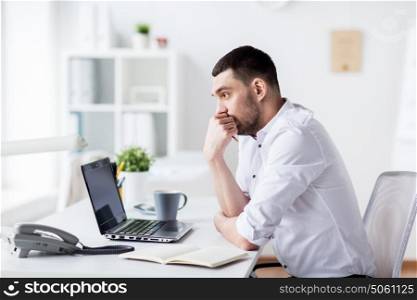 business and people concept - businessman with laptop and notebook sitting at office table and thinking. businessman with laptop and notebook at office