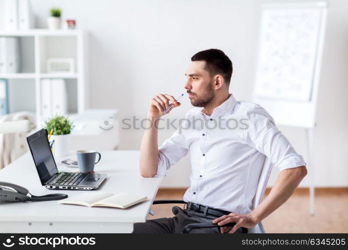 business and people concept - businessman with laptop and notebook sitting at office table and thinking. businessman with laptop and notebook at office