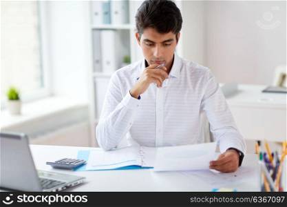 business and people concept - businessman with papers and laptop computer working at office. businessman working with papers at office