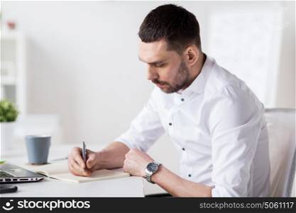 business and people concept - businessman writing to notebook at office. businessman writing to notebook at office
