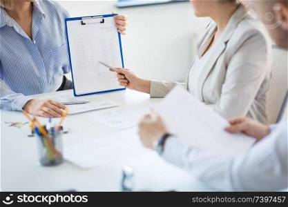 business and people concept - businesswoman showing clipboard with financial report to colleagues at office. business team discussing report at office