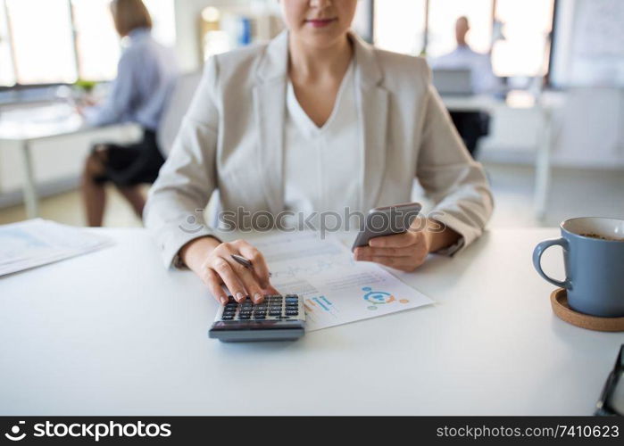 business and people concept - businesswoman with calculator, smartphone and papers working at office. businesswoman with calculator and smartphone