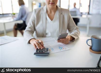 business and people concept - businesswoman with calculator, smartphone and papers working at office. businesswoman with calculator and smartphone