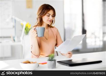 business and people concept - businesswoman with papers at working office and drinking coffee. businesswoman with papers drinks coffee at office. businesswoman with papers drinks coffee at office