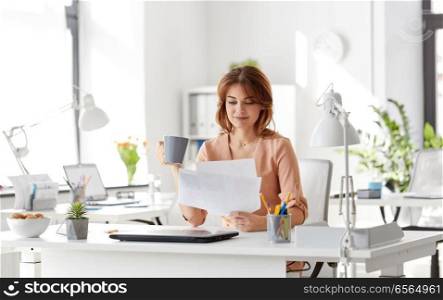 business and people concept - businesswoman with papers at working office and drinking coffee. businesswoman with papers drinks coffee at office