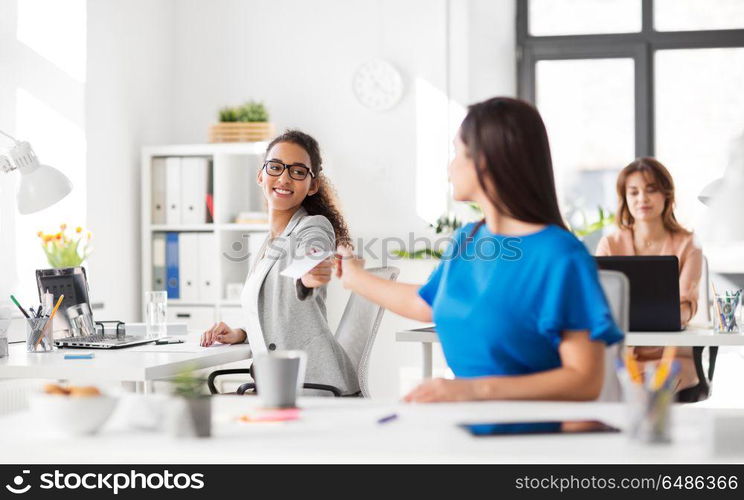 business and people concept - businesswomen giving each other papers at office. businesswomen giving each other papers at office. businesswomen giving each other papers at office