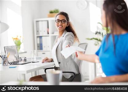 business and people concept - businesswomen giving each other papers at office. businesswomen giving each other papers at office. businesswomen giving each other papers at office