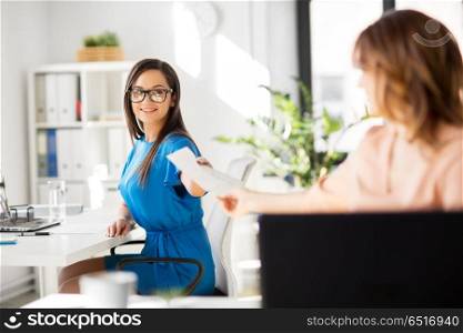 business and people concept - businesswomen giving each other papers at office. businesswomen giving each other papers at office. businesswomen giving each other papers at office