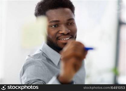business and people concept - close up of african american businessman writing something on glass board at office. businessman writing on glass board at office. businessman writing on glass board at office