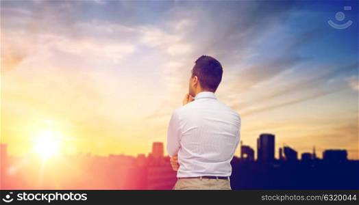 business and people concept concept - businessman thinking from back over city and sun light background. businessman thinking from back