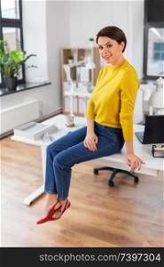 business and people concept - happy businesswoman sitting on desk at office. happy businesswoman sitting on desk at office