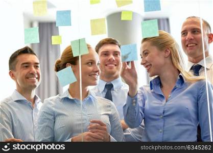 business and people concept - happy coworkers at glass wall with sticky notes. business team at glass wall with sticky notes