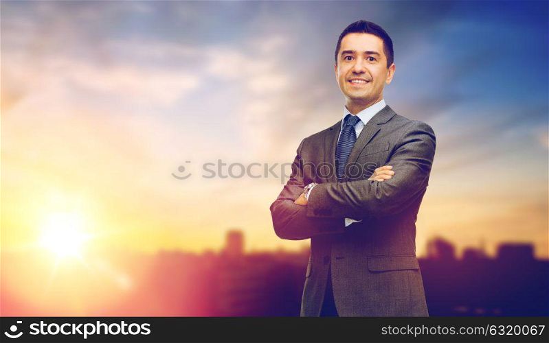 business and people concept - happy smiling businessman in suit over city and sun light background. happy smiling businessman over city background