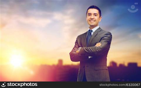 business and people concept - happy smiling businessman in suit over city and sun light background. happy smiling businessman over city background