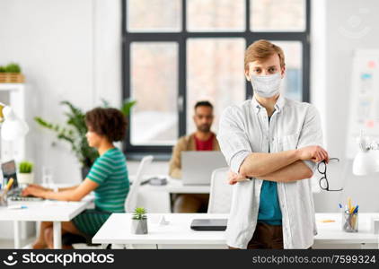 business and people concept - man with glasses wearing protective medical mask for protection from virus disease at office. man with glasses in medical mask at office