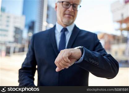 business and people concept - senior businessman checking time on his wristwatch in city. senior businessman with wristwatch on city street