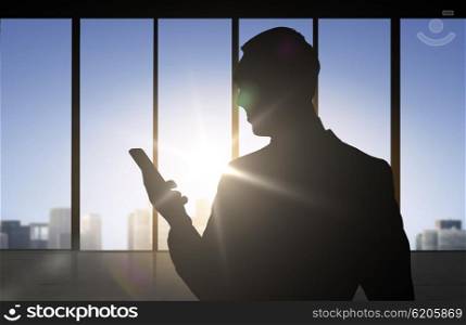 business and people concept - silhouette of businessman with smartphone over office window background. silhouette of businessman with smartphone
