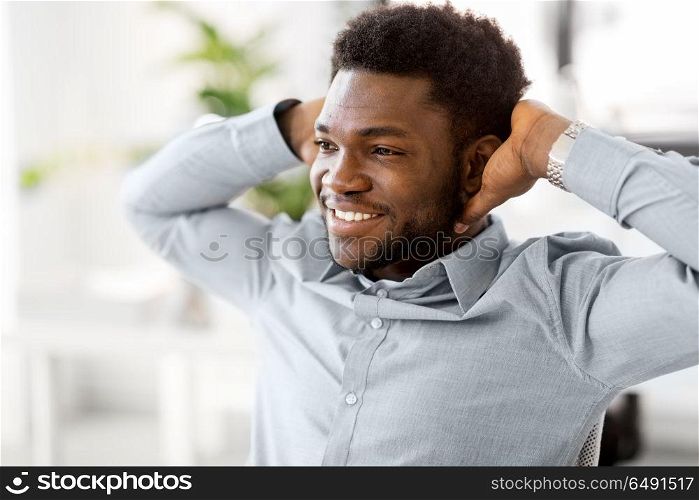 business and people concept - smiling african american businessman holding hands behind his head at office. smiling african american businessman at office. smiling african american businessman at office