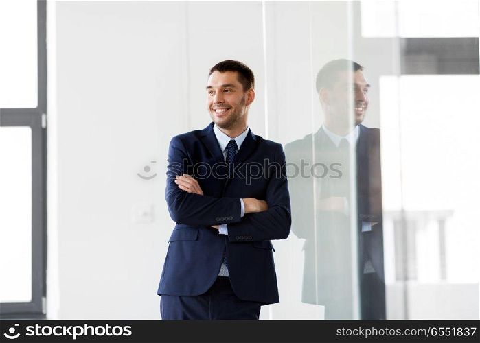 business and people concept - smiling businessman at office glass wall. smiling businessman at office glass wall. smiling businessman at office glass wall