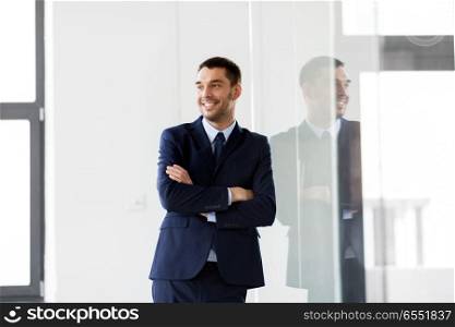 business and people concept - smiling businessman at office glass wall. smiling businessman at office glass wall. smiling businessman at office glass wall