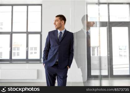 business and people concept - smiling businessman at office glass wall. smiling businessman at office glass wall