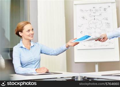 business and people concept - smiling businesswoman receiving papers from someone in office